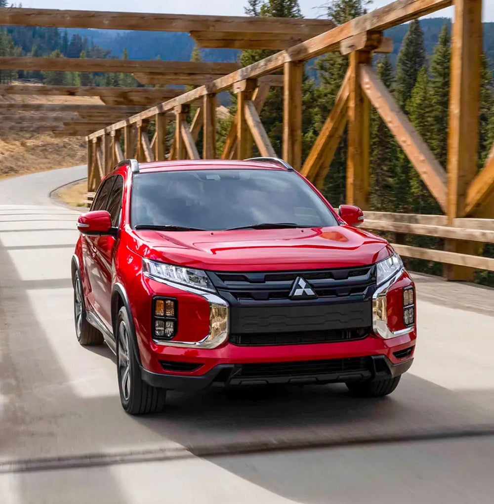 Red view of a red 2026 Mitsubishi Outlander Sport SUV driving across a bridge with wood crossbeams