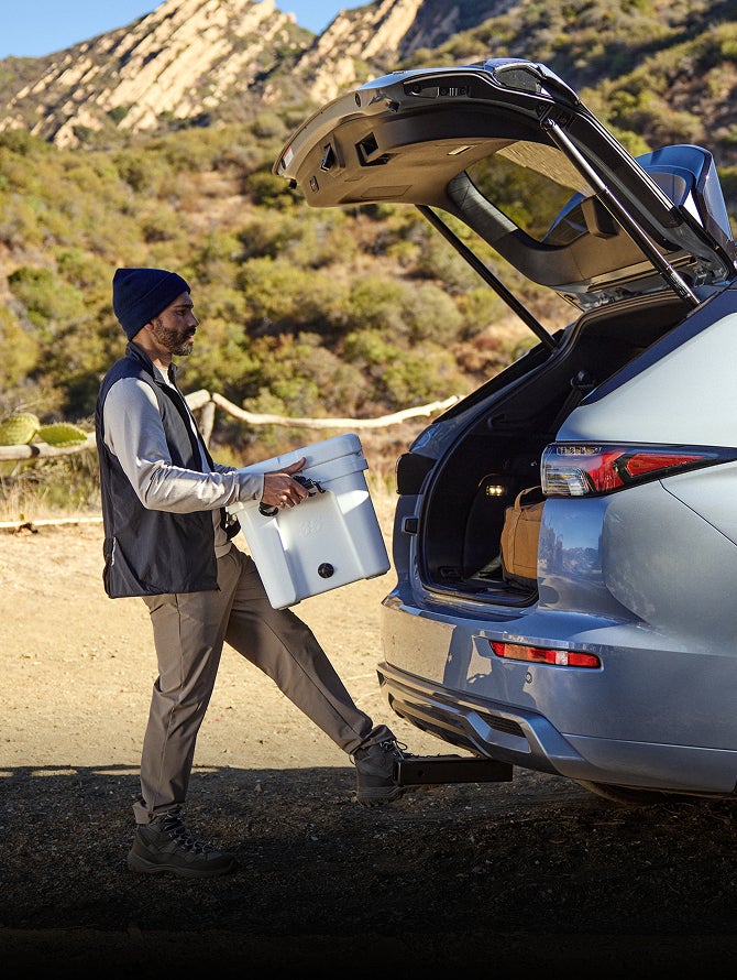 Person holding a box and using their foot to activate the Hands Free Power Liftgate in the 2026 Mitsubishi Outlander SUV