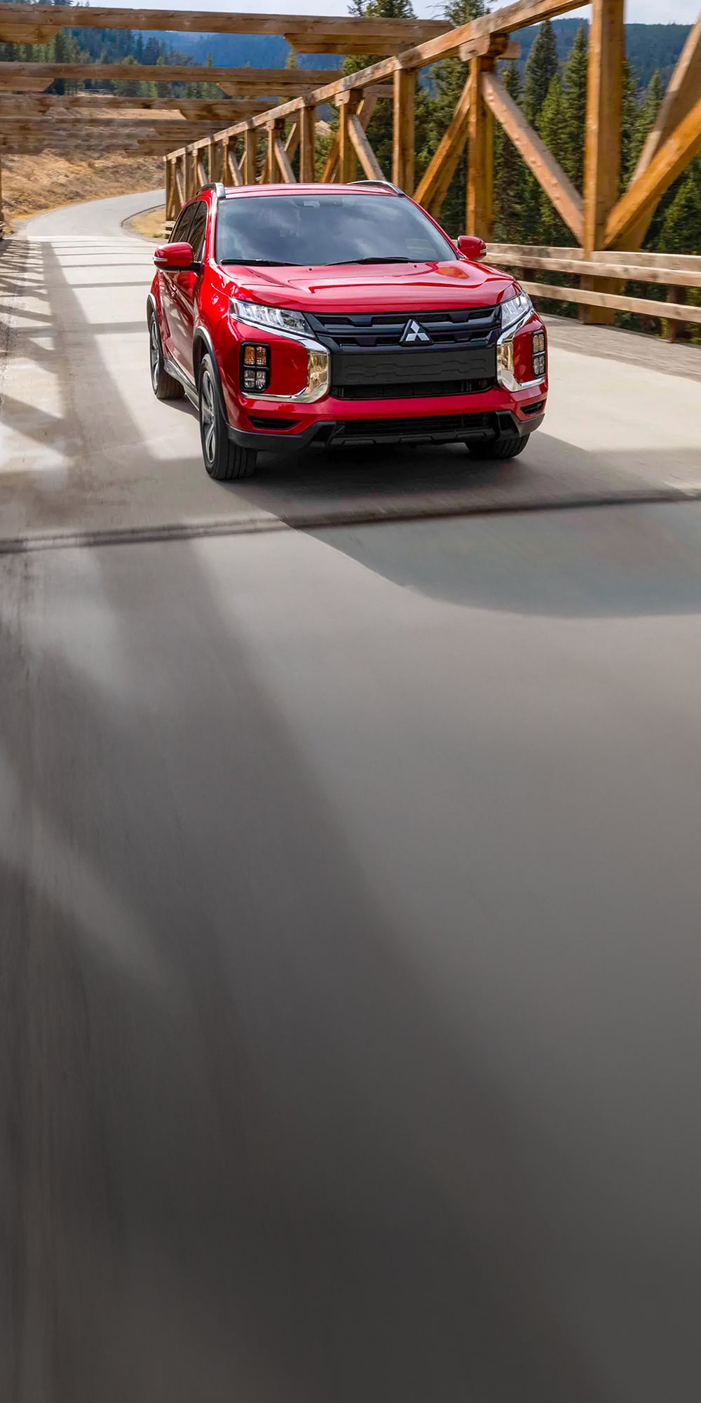 A red 2026 Mitsubishi Outlander Sport SUV driving on a bridge.