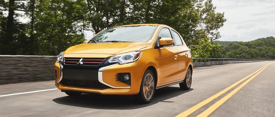 Yellow 2024 Mitsubishi Mirage Compact Hatchback driving on a highway lined with trees