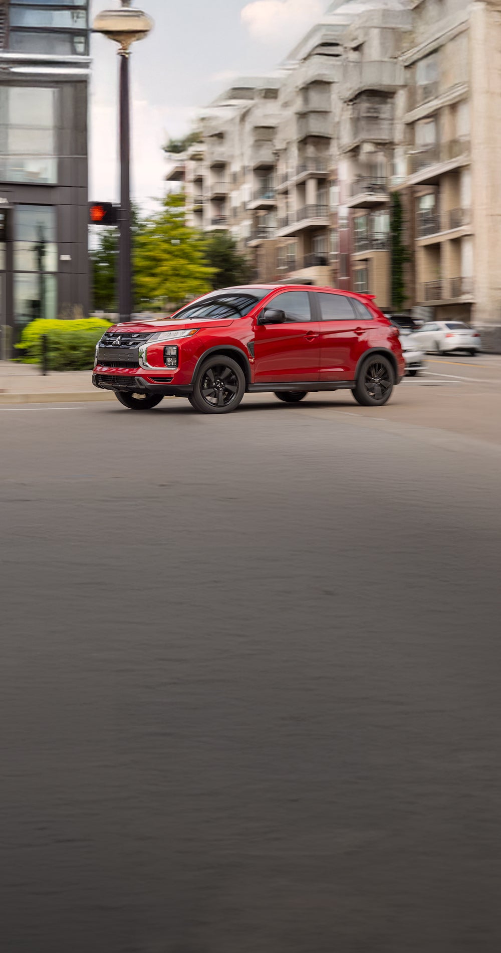 Side profile of a red 2026 Mitsubishi Outlander Sport SUV driving on a city street