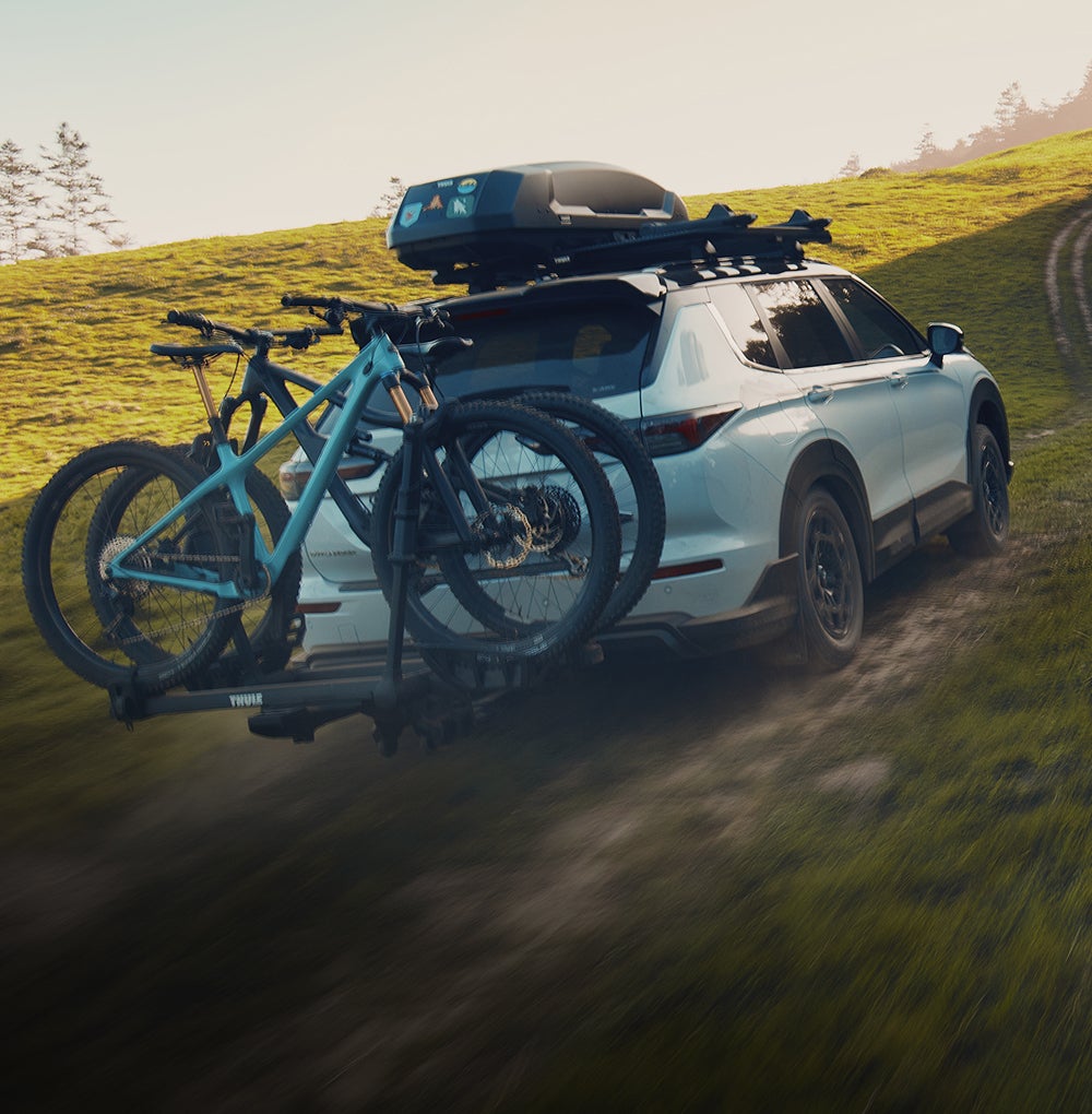2026 Mitsubishi Outlander SUV Trail Edition driving off road with two bikes on a rear mounted bike rack